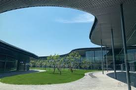 Modern building with a curved roof, large glass windows, and a courtyard with grass and small trees.
