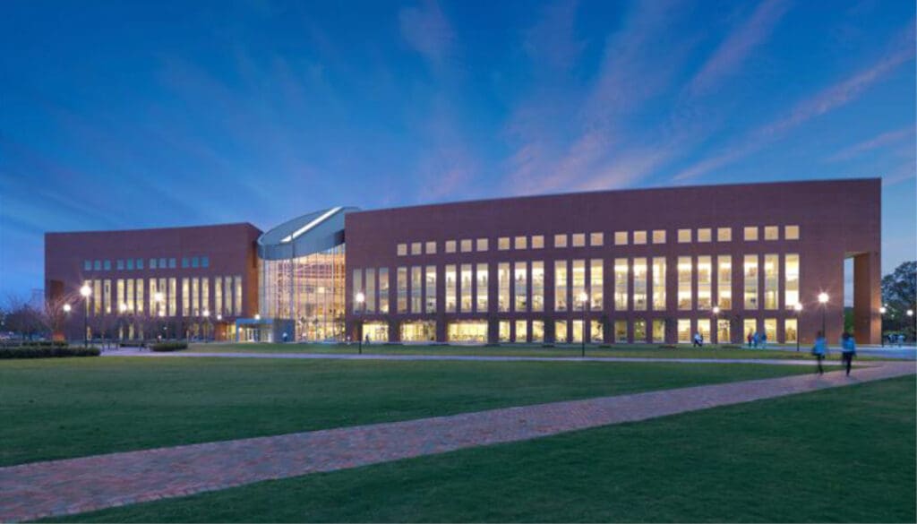 Modern building with large glass windows, central entrance, green lawn, pathways, and dusk sky.