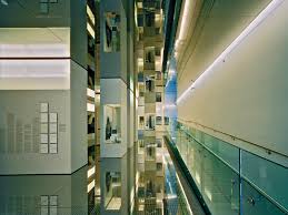 Modern multi-story building interior with glass railings, illuminated walls, and reflective surfaces.