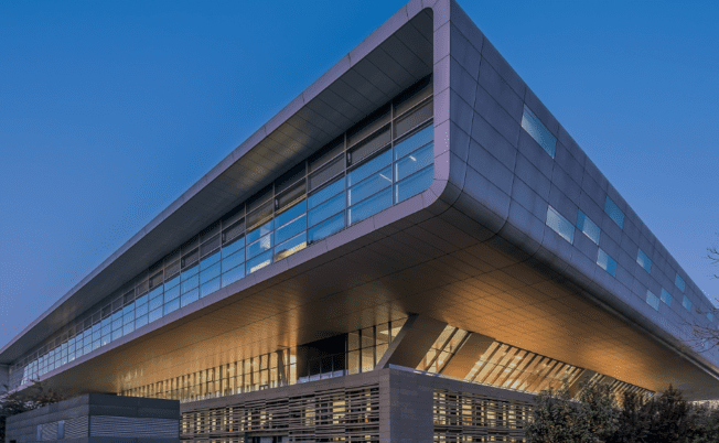 Modern building with angled overhangs, glass, and metal exterior against clear twilight sky.