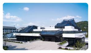 Modern building with large glass windows, slanted roofs, and landscaped surroundings against clear skies.
