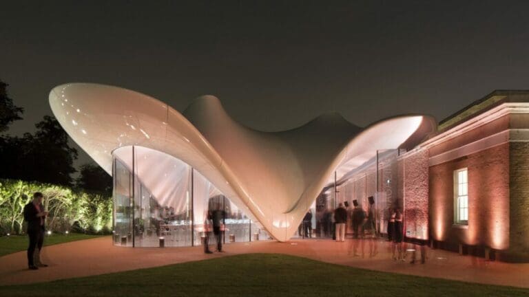 Modern building with wave-like roof, glass walls, brickwork, and people gathered at night.