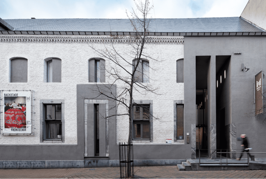 Modern building with white and gray facade, poster, leafless tree, walking person, and brick pavement.