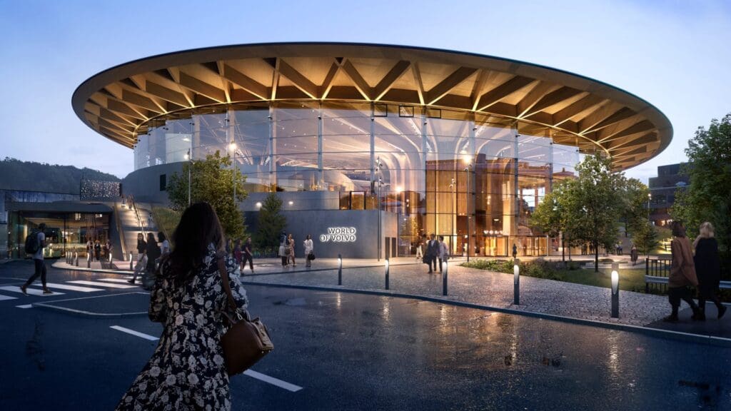 Modern circular glass building with wooden roof, evening, illuminated within, "World of Volvo".