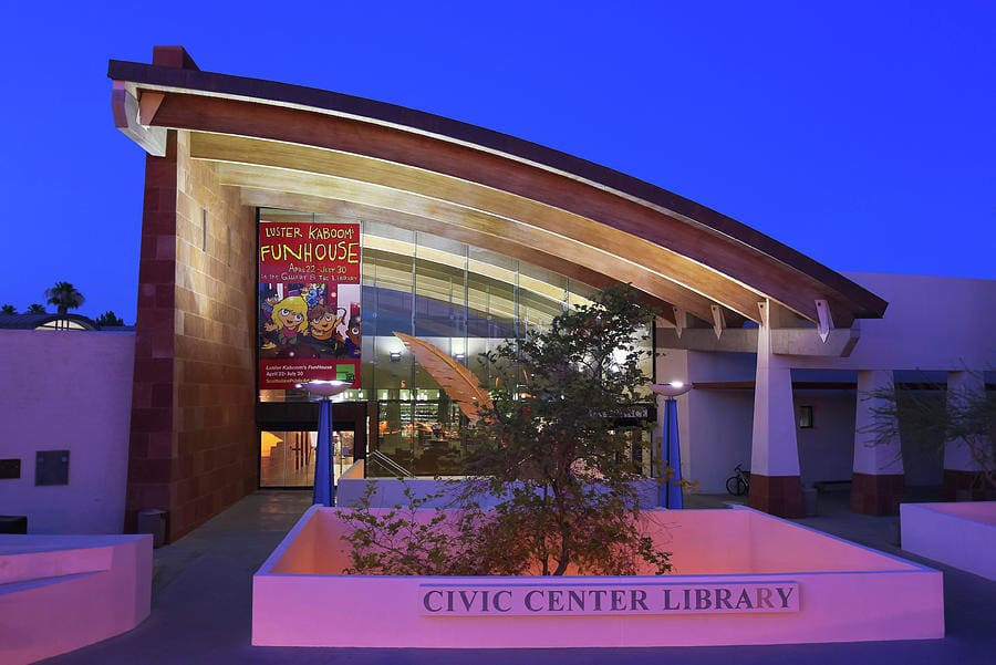 Modern Civic Center Library with arched wooden roof, glass windows, Funhouse event sign, twilight sky.