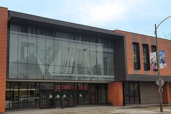 Modern two-story commercial building with glass facade, orange-gray panels, and streetlight banners.