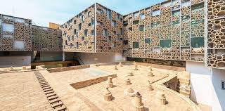 Modern building with cylindrical facade elements, numerous windows, surrounding a minimalist courtyard.