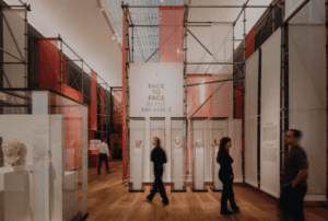 Modern exhibition space displaying Roman sculptures and artifacts from 100-44 BCE with visitors observing.