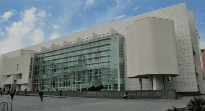 Modern glass façade building, Museum of Contemporary Art in Barcelona, people in front plaza, cloudy sky.