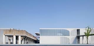 Modern building with white structures and glass next to an industrial concrete structure, blue sky.