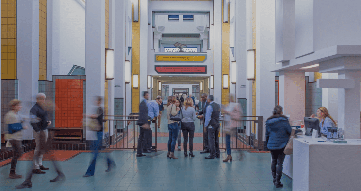 Modern indoor hallway with people conversing, colorful tiles, tall white walls, and a receptionist.