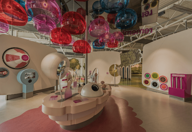 Modern interactive exhibition with colorful overhead spheres, curved white structures, and displays.
