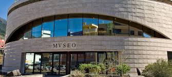 Museum with modern curved façade, arch-shaped windows, "MVSEO" sign, plants, sunny sky background