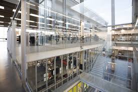 Modern multi-level office with glass walls, open workspaces, stairs, and bright lighting.