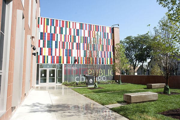 Modern public building with colorful geometric facade, glass doors, paved walkway, lawn, and benches.