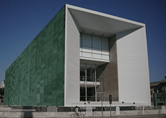Modern rectangular building with green-tiled facade, white-framed entrance, and large glass windows.