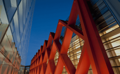 Modern structure with red lattice framework and glass facade at dusk with deep blue sky.