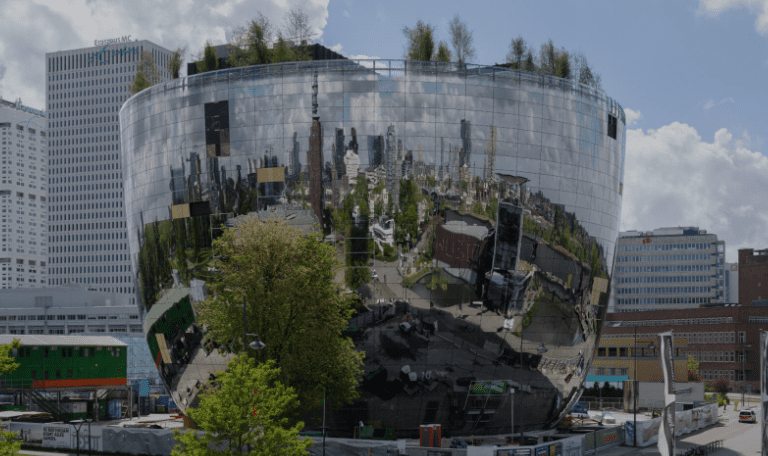 Modern reflective bowl-shaped building with surrounding cityscape mirrored on its surface.