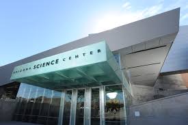 Entrance of a modern science center with a glass facade and prominent identifying sign.