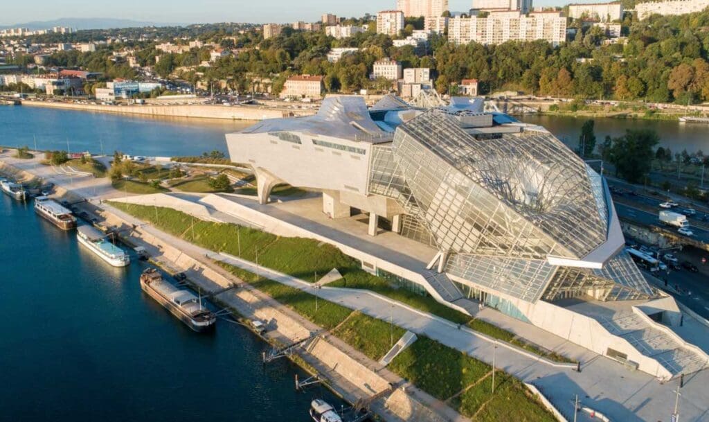 Modern waterfront building with glass and concrete design, docked boats, and urban background.