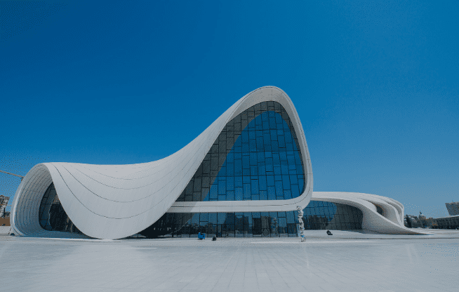 Modern building with fluid, wave-like design and extensive glass windows against a clear blue sky.