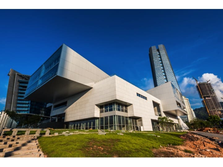 Modern white architectural complex with sharp angles and glass, skyscraper in background, green lawn