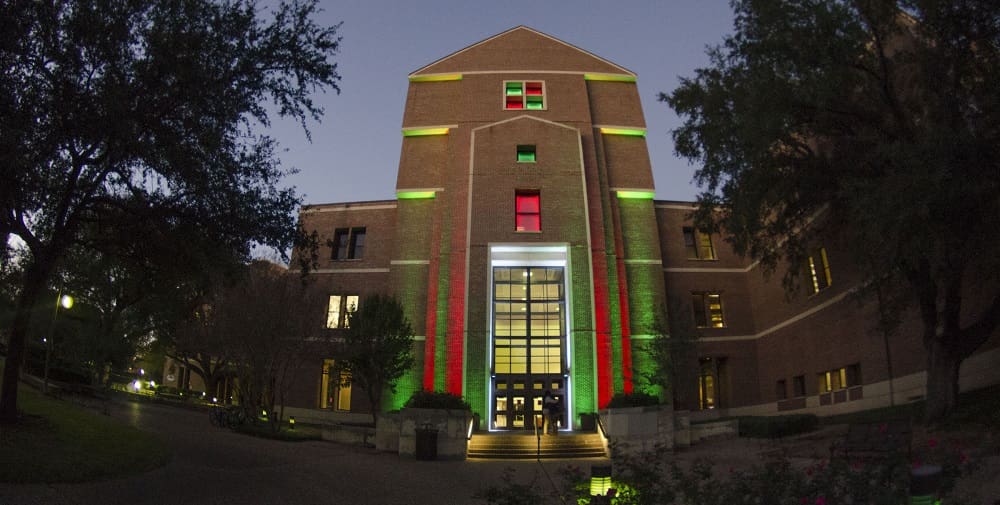 Multi-story brick building illuminated at night with red and green lights, central glass entrance.