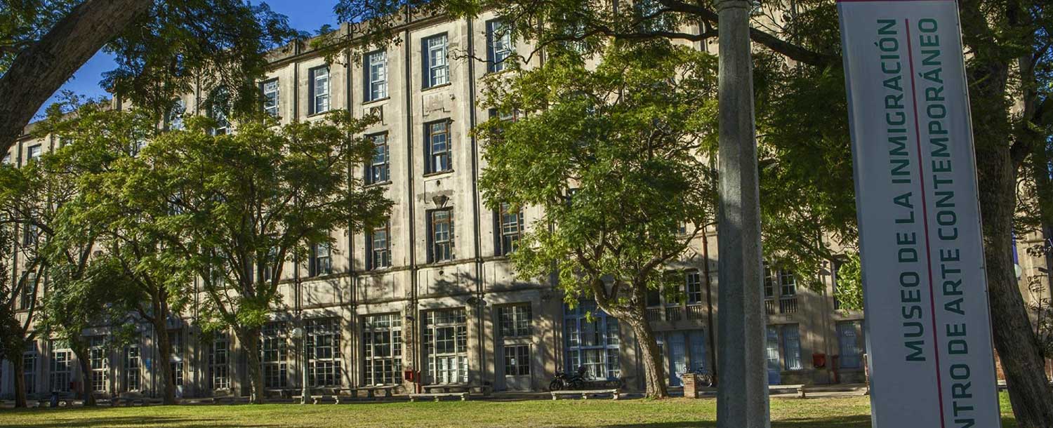 Multi-story building with mature trees, foreground sign for Museo de la Inmigración and art center.