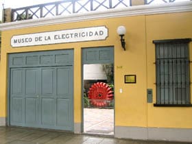 Exterior of Museo de la Electricidad with yellow walls, blue doors, and a red gear visible inside.