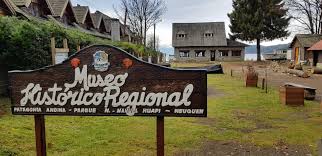 Wooden sign for Museo Histórico Regional in scenic area with traditional buildings, trees, mountains.