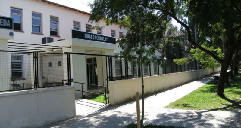 Entrance to Museo Icholay with metal gate and fence, surrounded by trees and sidewalk.