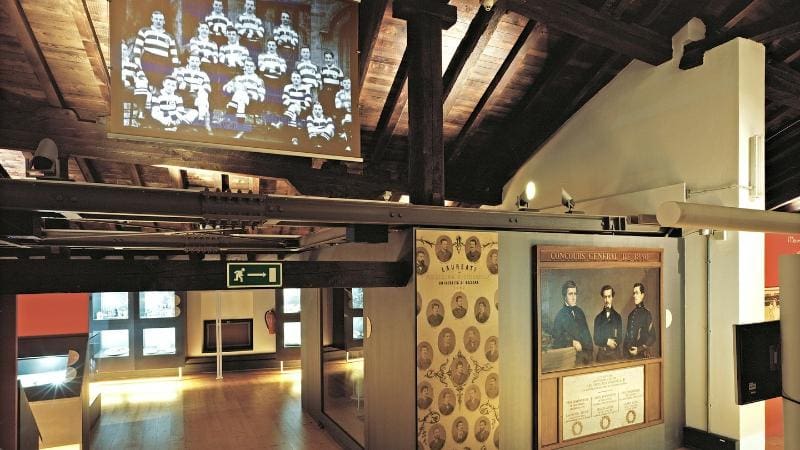 Museum exhibit room with wooden floors, display cases, historical photos, and a projected group photo.
