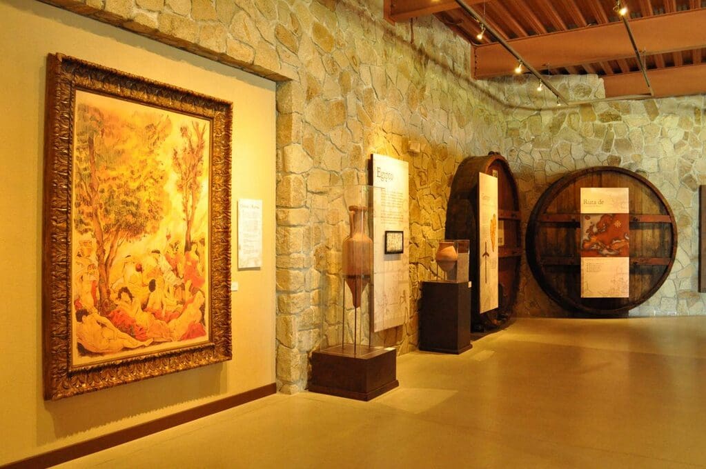 Museum exhibit with stone walls, large painting of trees and people, informational panels, artifacts.