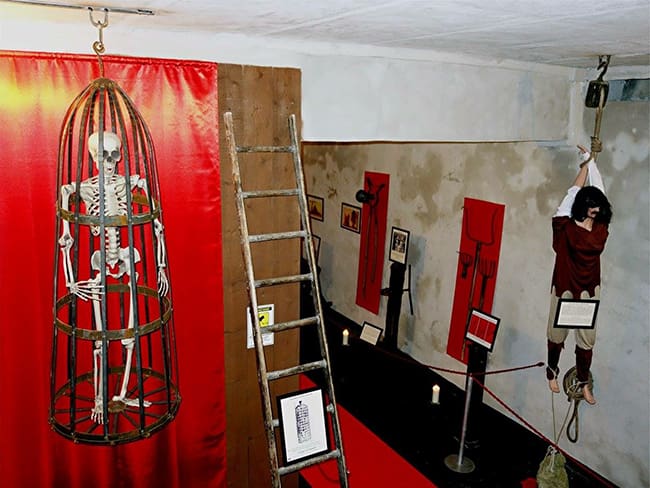 Museum exhibit with historical torture devices, including a skeleton and mannequin in restraints.