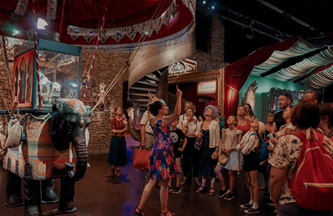 Guide speaking to a group inside a museum with a decorative elephant display and festive decor.