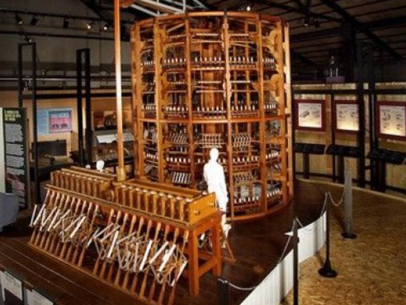 Museum exhibit of a large wooden industrial machine with mannequin and informational displays.