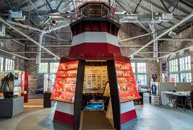 Museum exhibit of a large red and white lighthouse model with open sections displaying artifacts.