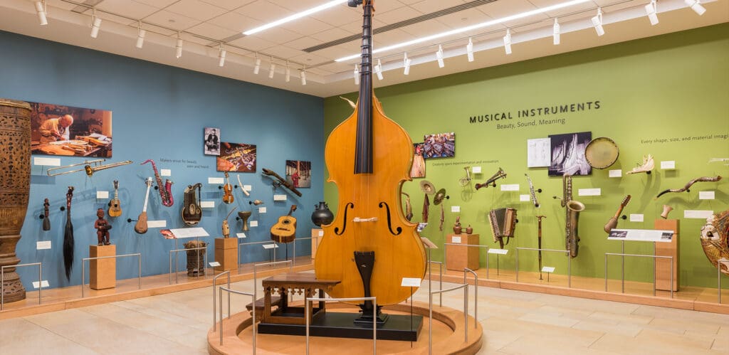 Museum exhibit featuring various musical instruments on blue and green walls with a large double bass