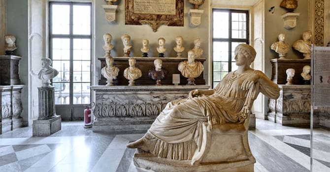 A museum room with classical sculptures, including a large seated woman statue and several busts.