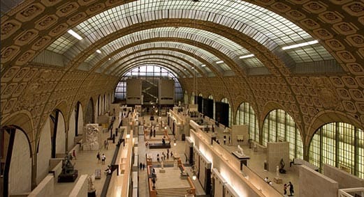 Vaulted hall with ornate glass ceiling in museum, filled with exhibits, sculptures, and visitors.