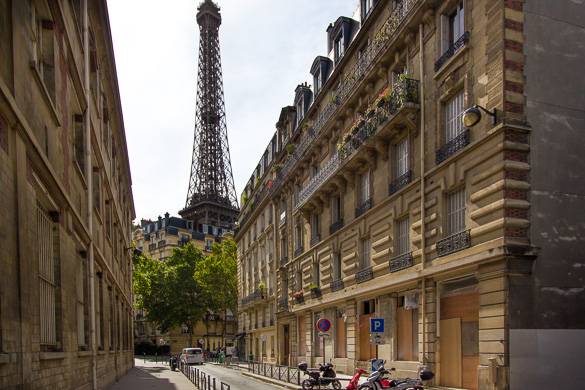 Narrow Paris street with traditional buildings, stone facades, parked scooters, and Eiffel Tower.