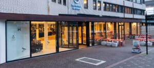Nationaal Archief exterior with glass windows, bright entrance, tables, stools, and signage outside.