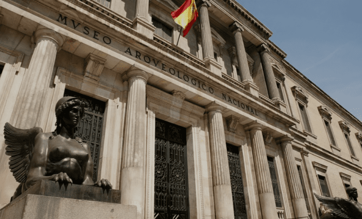 Entrance of the National Archaeological Museum in Madrid with columns, statues, and a Spanish flag.