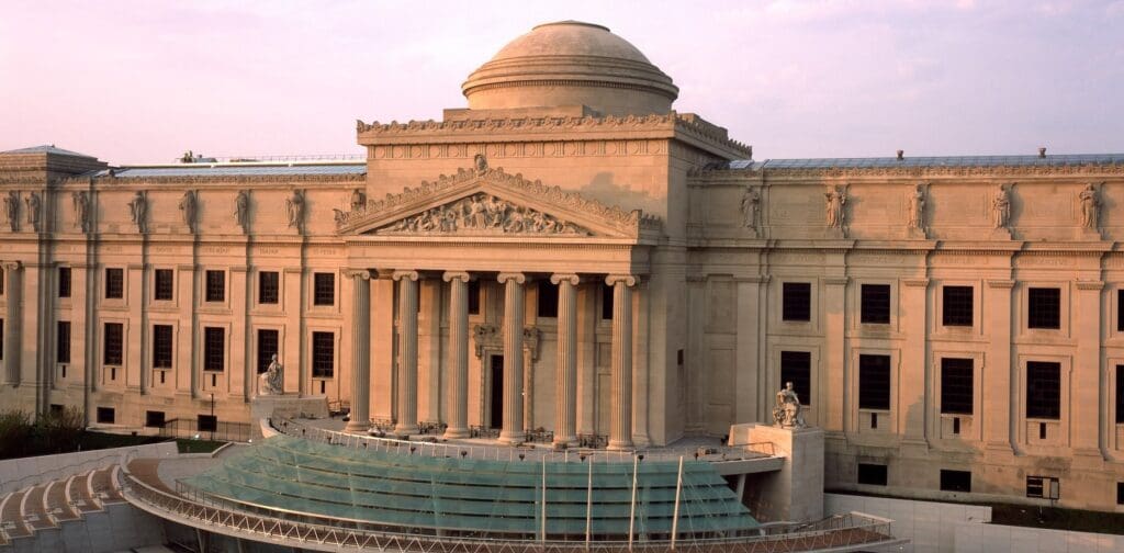Neoclassical building with columns, domed roof, sculptures, and an external amphitheater with tiered seating.