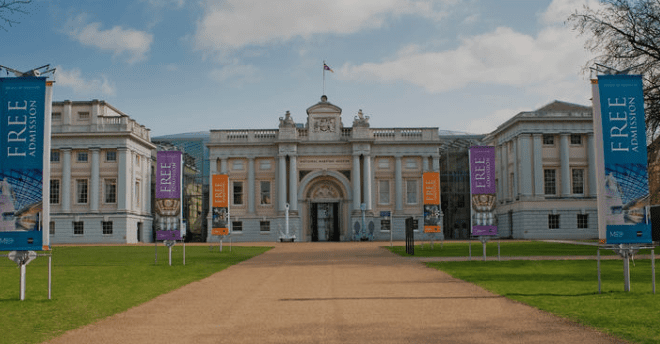 Large neoclassical museum building with central dome, banners promote free admission, grassy lawn.