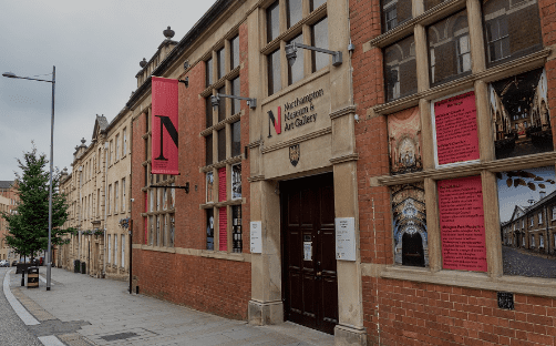Exterior of Northampton Museum & Art Gallery with red-brick facade, signage, and banners along a street.