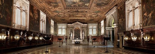 Spacious, ornately decorated hall with frescoes, paintings, statues, and classical architectural elements.