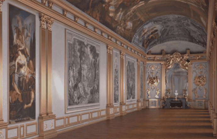 Ornate hall with high arched ceiling, intricate paintings, gilded columns, and polished wood floor.