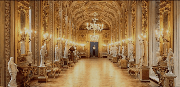 Ornate hall with golden ceiling, chandeliers, classical statues, mirrors, and polished wooden floor.