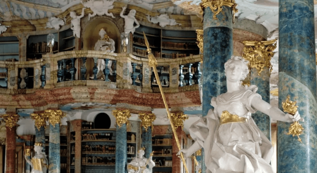 ornate interior with marble columns, gold accents, statues, multi-tiered balcony, and library shelves